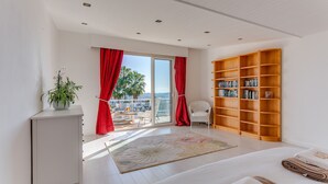 Ein modernes Schlafzimmer mit großem Fenster, einer Holzbücherreol, einem weißen Kleiderschrank und einem Balkon mit roten Vorhängen.