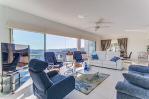 A spacious living room with a large TV, comfortable seating, a coffee table, and a view of the city. - VILLA LOUPA VI4489 by Riviera Holiday Homes (La Colle-sur-Loup)