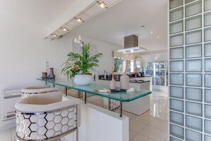 A modern kitchen with a glass dining table, white cabinetry, and a large window. - VILLA LOUPA VI4489 by Riviera Holiday Homes (La Colle-sur-Loup)