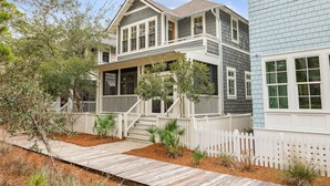 A two-story house with a covered porch, a white picket fence, and a wooden deck. - Peaceful family friendly coastal oasis with room to unwind, play, and reconnect (Watersound West)