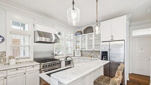 A kitchen with white cabinetry, stainless steel appliances, a marble island, wicker chairs, and pendant lighting. - Peaceful family friendly coastal oasis with room to unwind, play, and reconnect (Watersound West)