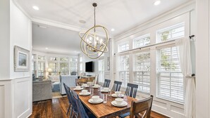 A dining area with a wooden table set for six, surrounded by blue chairs, in a room with white walls and wooden floors. - Peaceful family friendly coastal oasis with room to unwind, play, and reconnect (Watersound West)