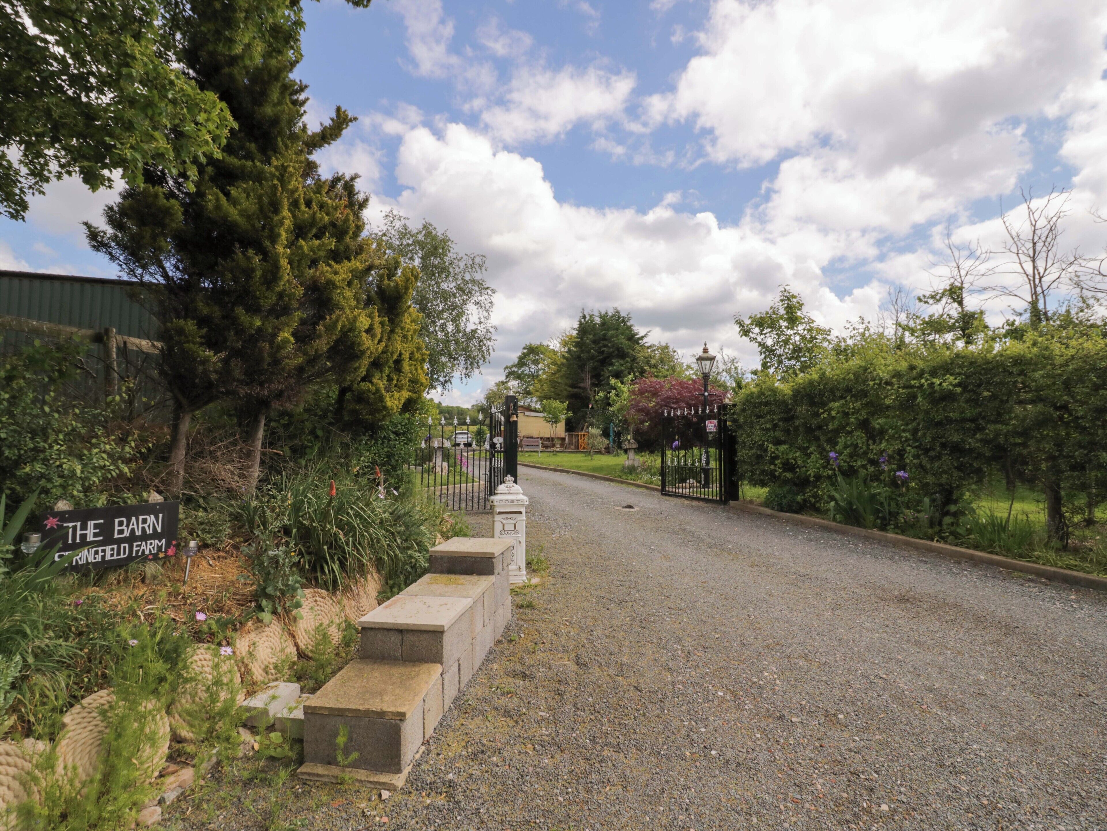 Une allée de gravier mène à une entrée fermée par un portail sur lequel on peut lire : « The Barn Ringfield Farm ».