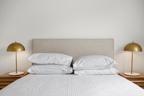 Ein ordentlich gemachtes Bett mit weißen Leinen und zwei goldenen Lampen auf Holznachtischen.