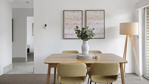 A dining area with a wooden table, two chairs, a vase with greenery, and two framed artworks on the wall. - Spacious 2-bed Apartment Near City Centre (Brisbane)