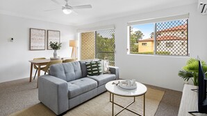 A modern living room with a grey sofa, a dining table with chairs, a coffee table, and a TV. - Spacious 2-bed Apartment Near City Centre (Brisbane)