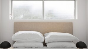 A bed with white bedding and a beige headboard, positioned under a window with frosted glass. - Spacious 2-bed Apartment Near City Centre (Brisbane)