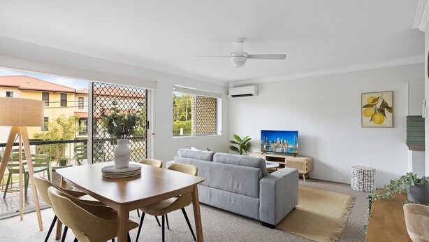 A modern living room with a dining area, grey sofa, wooden table, and a ceiling fan. - Spacious 2-bed Apartment Near City Centre (Brisbane)