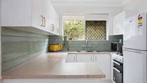 A modern kitchen with white cabinets, a granite countertop, a yellow kettle, a microwave, and a refrigerator. - Spacious 2-bed Apartment Near City Centre (Brisbane)