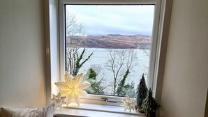Ein Fenster mit Blick auf einen See und Hügel, ein weißes Kissen und ein dekoratives Schneeflockenmuster.