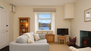 Ein gemütliches Wohnzimmer mit einer Couch, einem Fernseher, einem Kamin, einem Bücherregal und einem Fenster mit Seeblick.