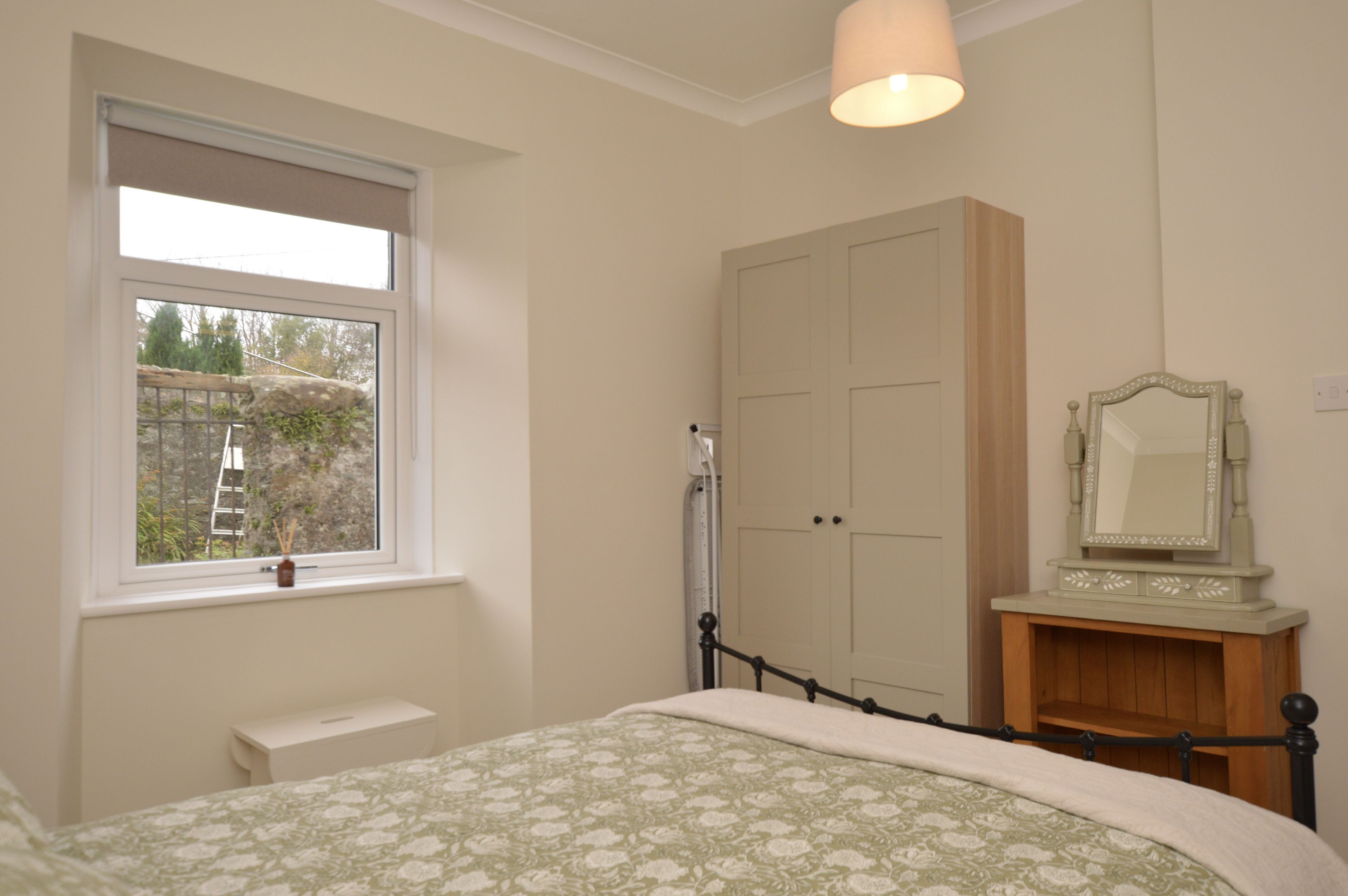 A bedroom with a bed, a window, a wardrobe, and a mirror.