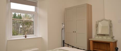 A bedroom with a bed, a window, a wardrobe, and a mirror.