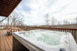 Ein Whirlpool auf einer Holzterrasse mit Blick auf Bäume und Berge im Hintergrund.