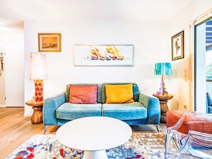 A living room with a blue sofa, a white coffee table, and a colorful rug. There are two lamps on side tables, and a framed picture on the wall. - Apartment Xarako by Interhome (Urrugne)