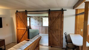 Een kamer met een houten bank, een bureau met stoel, en een schuifdeur van hout die leidt naar een andere kamer.