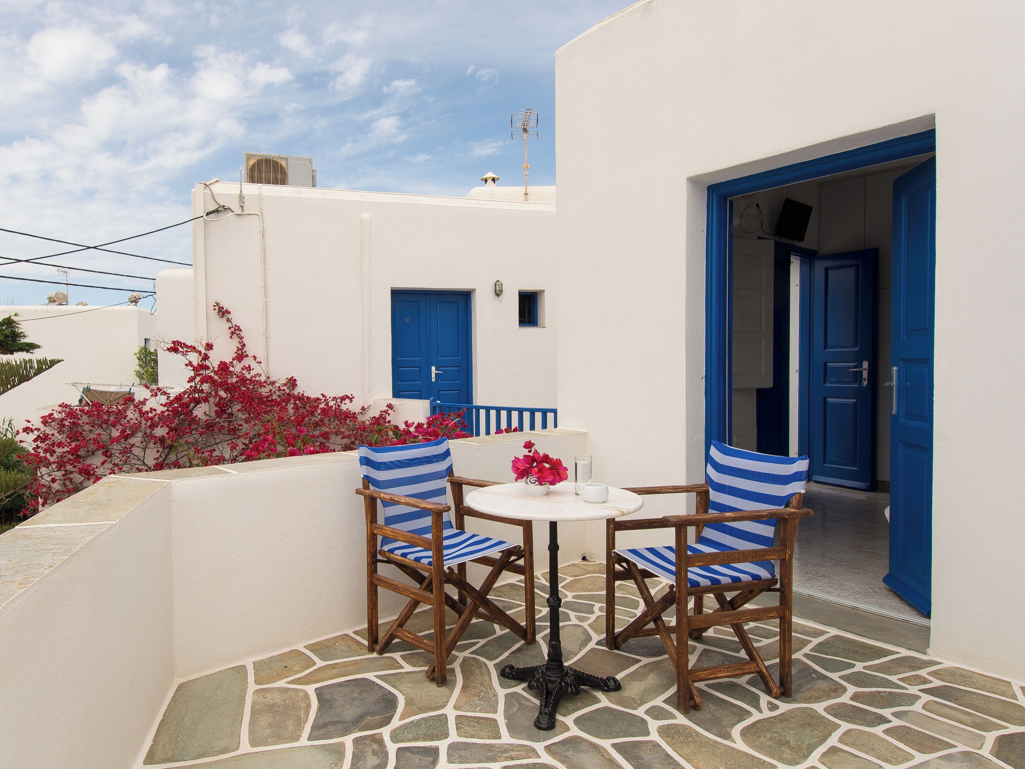Un edificio blanco con puertas y ventanas azules, suelo de piedra y una mesa con sillas.