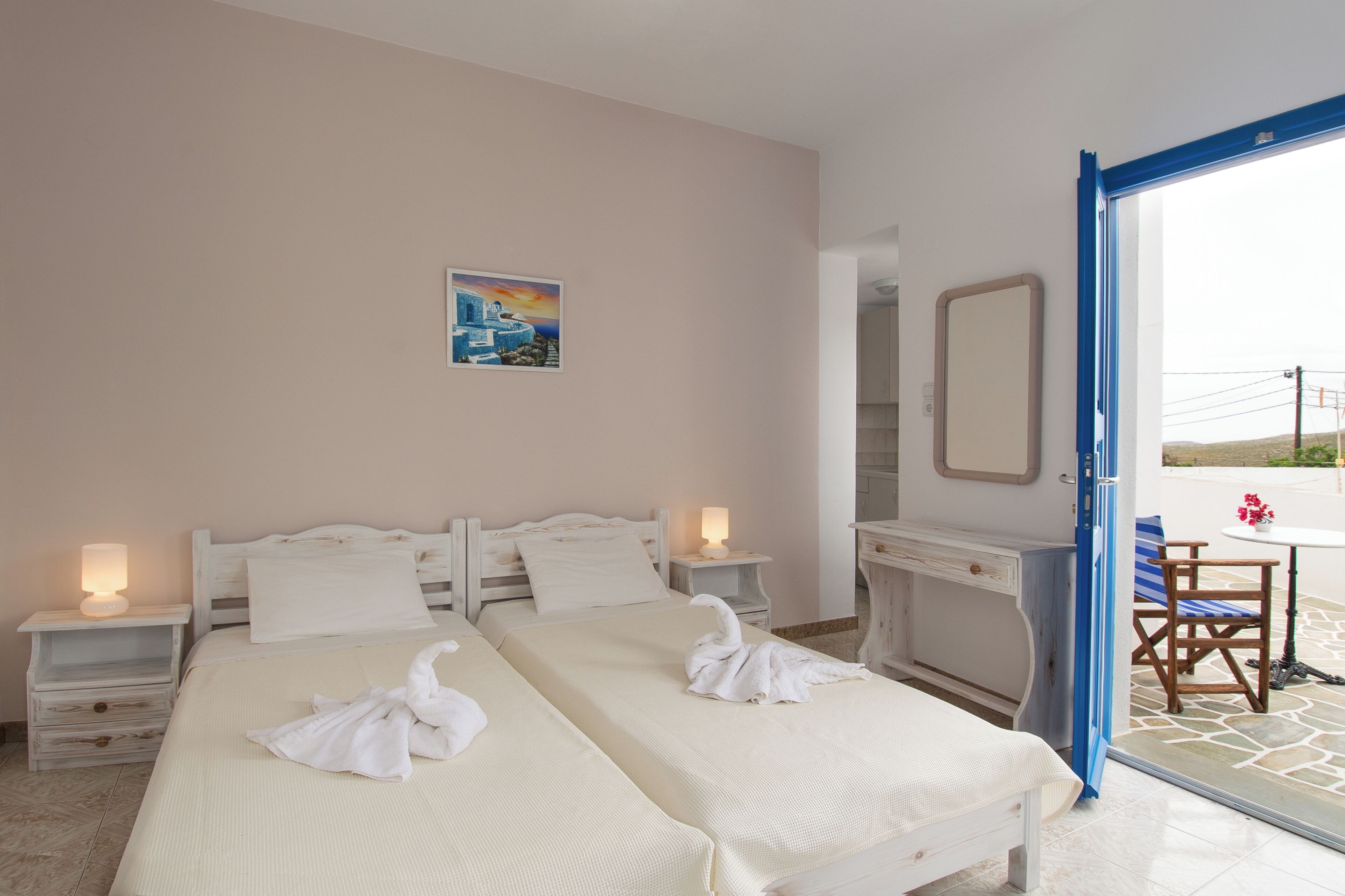 A hotel room with two beds, a desk, a chair, and a table with a view of the outside.