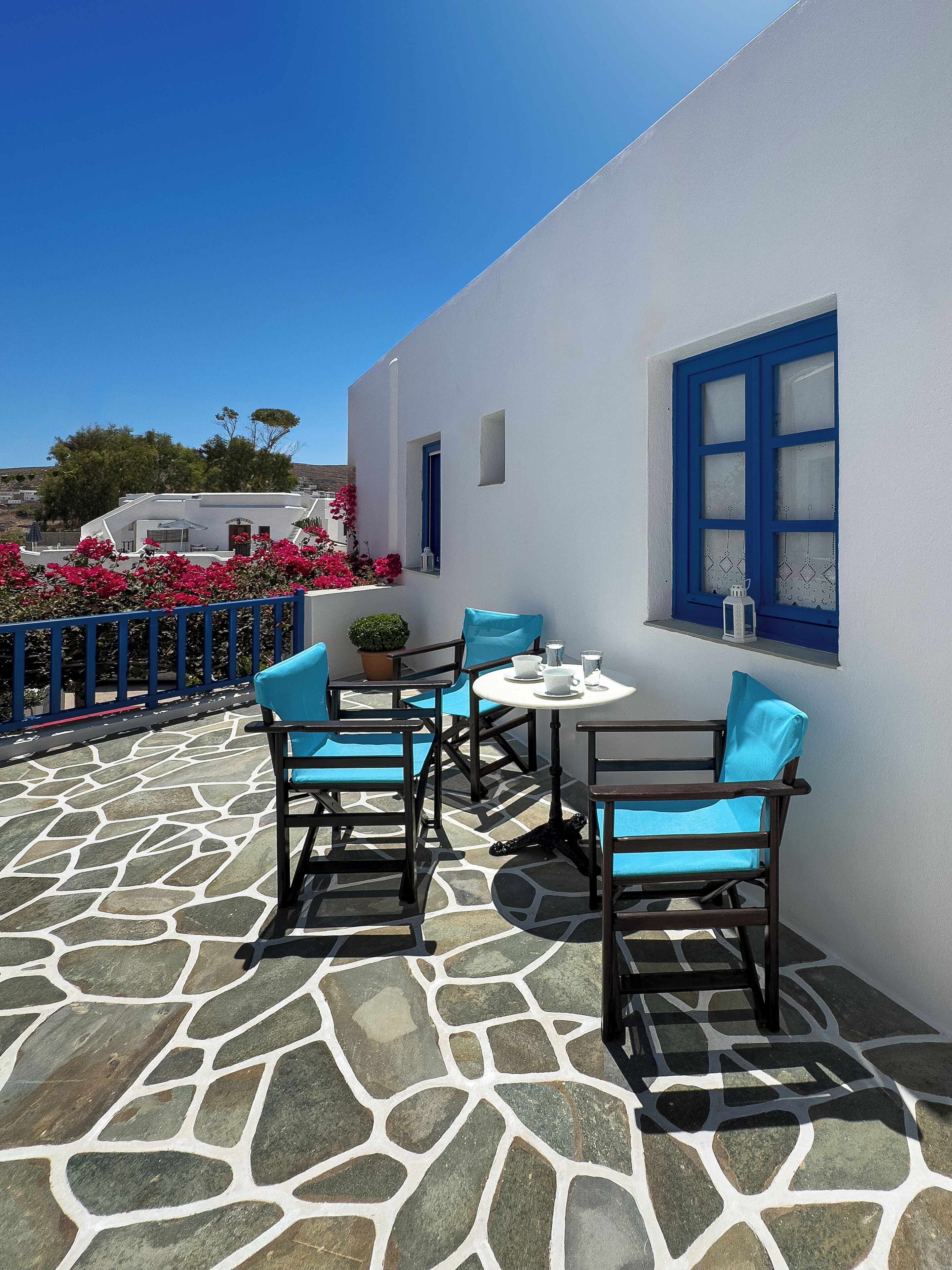 Una terraza con suelo de piedra, muebles azules y paredes blancas.