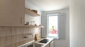 Eine Küche mit doppelter Spüle, einem Fenster mit geöffneten Fensterläden und einem Holzer Schneidebrett auf der Arbeitsfläche.
