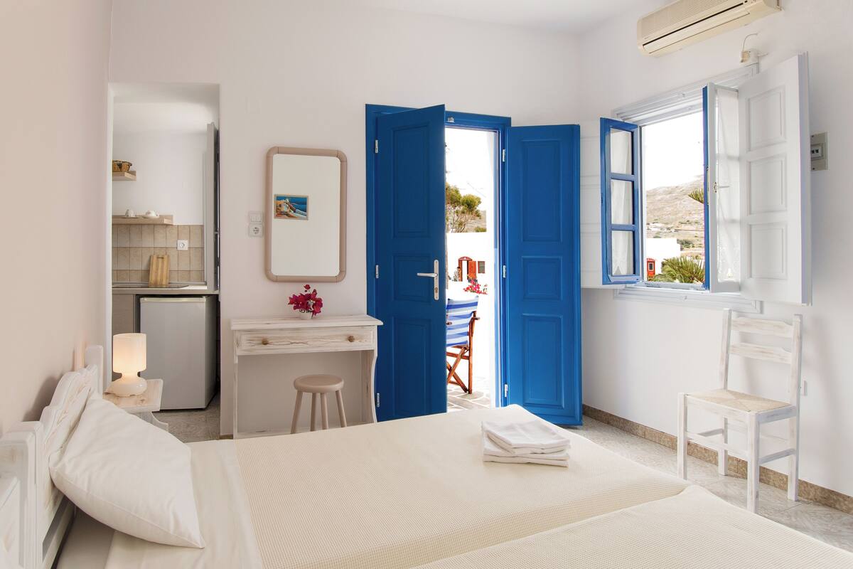 A bedroom with a bed, a desk, a chair, and an open door leading to a balcony.