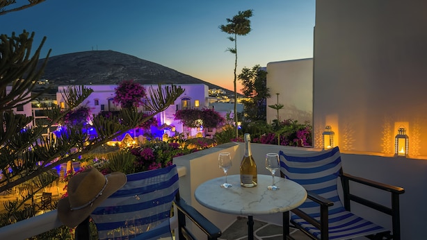 Eine Terrasse mit Tisch und Stühlen, einer Weinflasche und Blick auf ein Gebäude mit beleuchteten Fenstern.
