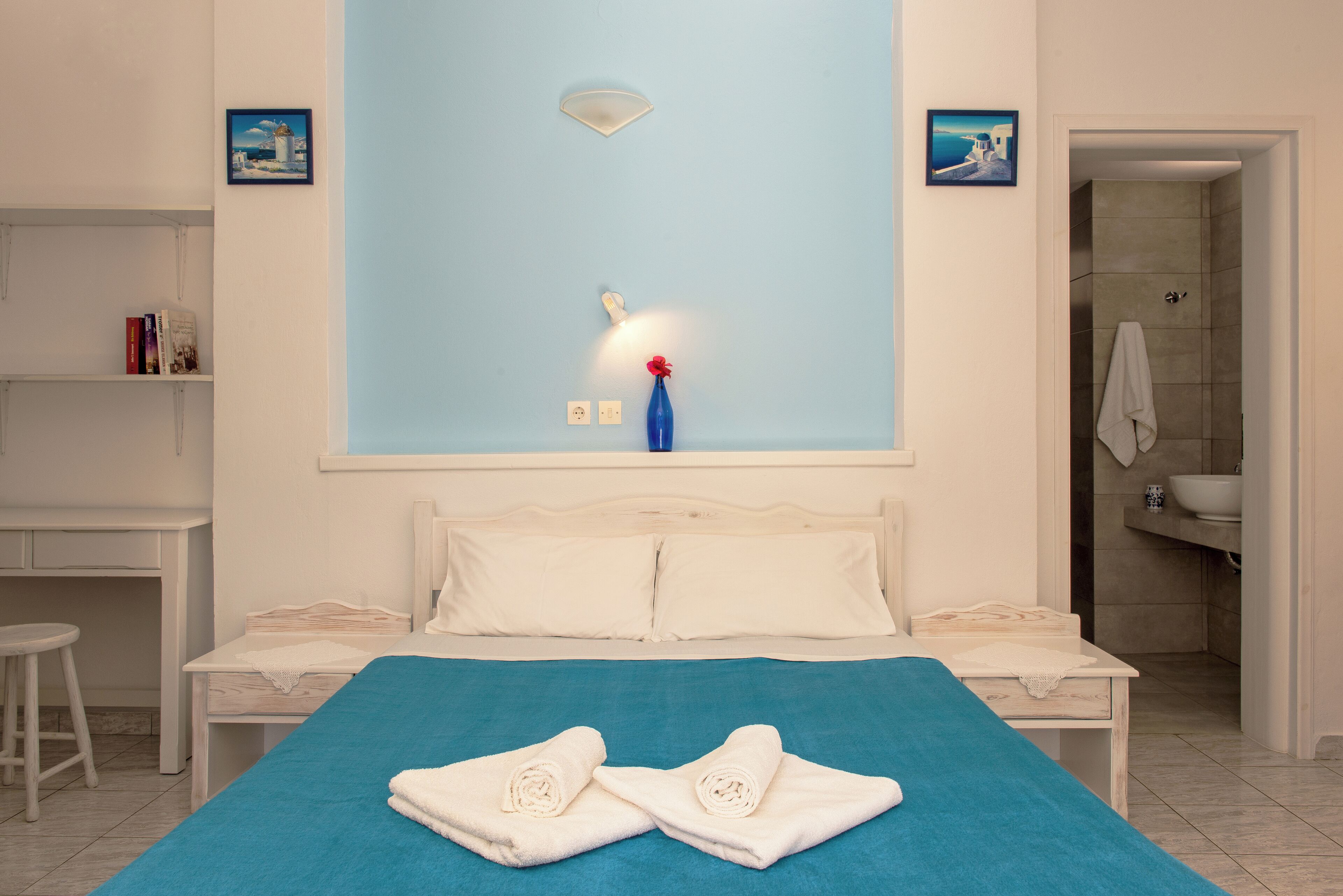 Un dormitorio con cama, escritorio y baño a la vista a través de una puerta abierta.