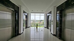 A modern hallway with marble walls, a polished floor, and large windows offering a view of the city. - Apartemen Poris 88 by Linkara (Tangerang)