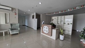A reception area with a reception desk, a grey armchair, a white table, and a potted plant. - Apartemen Poris 88 by Linkara (Tangerang)