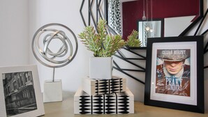 Een modern interieur met een metalen geometrisch beeldhouwwerk, een pot met een vetplant, een ingelijste foto en een trap met een geometrisch hekwerk.