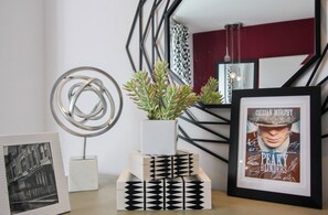 Ein modernes Interieur mit einer geometrischen Metallskulptur, einer Topfpflanze mit Sukkulenten, einem gerahmten Foto und einer Treppe mit geometrischer Geländerkonstruktion.