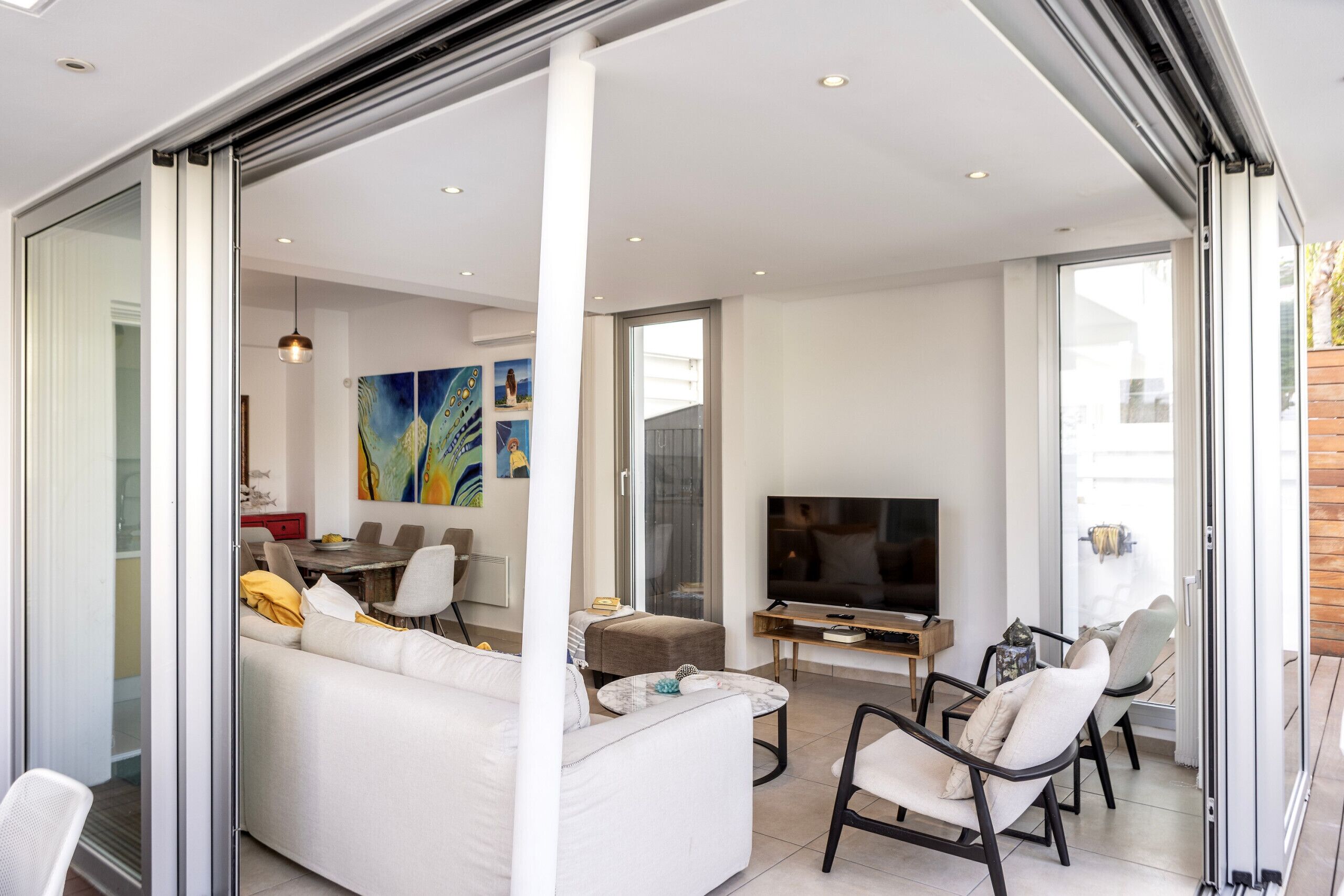 Un salon moderne avec un canapé blanc, un téléviseur et un coin repas comprenant une table et des chaises.