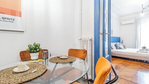 Une chambre moderne avec une table en verre, des chaises orange, un lit avec une tête de lit bleue et un appareil de climatisation blanc.