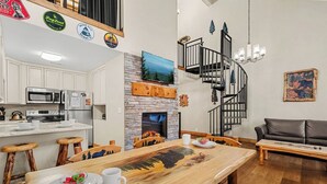 A modern kitchen with white cabinets, a stone fireplace, and a dining area with a wooden table and chairs. - 2 BD Gatlinburg Condo | Walk To Town | Sleeps 8 (Gatlinburg)