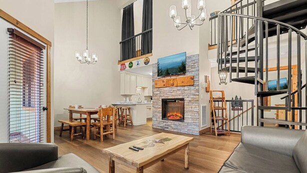 A modern living room with a fireplace, a dining area, and a staircase. - 2 BD Gatlinburg Condo | Walk To Town | Sleeps 8 (Gatlinburg)