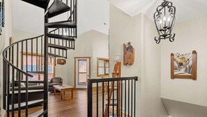 A spacious living area with a wooden staircase, a black railing, and a chandelier. - 2 BD Gatlinburg Condo | Walk To Town | Sleeps 8 (Gatlinburg)