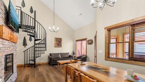 A spacious living area with a wooden dining table, black leather sofa, and a spiral staircase. - 2 BD Gatlinburg Condo | Walk To Town | Sleeps 8 (Gatlinburg)