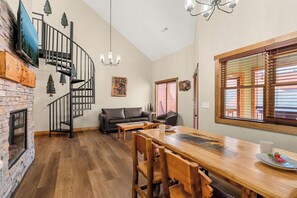 A spacious living area with a wooden dining table, black leather sofa, and a spiral staircase. - 2 BD Gatlinburg Condo | Walk To Town | Sleeps 8 (Gatlinburg)