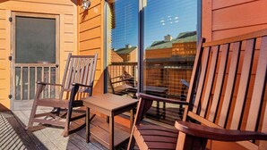 A wooden deck with a table and chairs, a sliding glass door, and a view of buildings in the background. - 2 BD Gatlinburg Condo | Walk To Town | Sleeps 8 (Gatlinburg)