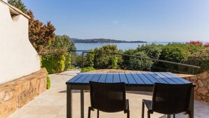 Een terras buiten met een tafel en twee stoelen, met uitzicht op een schilderachtig waterlandschap en land in de verte.