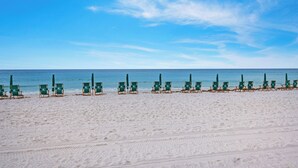 Une plage bordée de rangées de chaises longues vertes et de parasols.