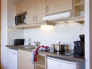 A compact kitchen with wooden cabinets, a microwave, a kettle, a coffee maker, and a dishwasher. - Odalys Référence Le Grand Panorama 1 by Interhome (Valmeinier)