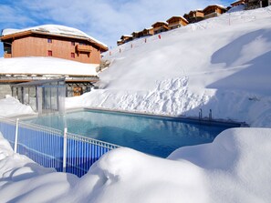Ein Pool, umgeben von Schnee, Holzhäusern und einer Skipiste.