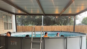 En pool som står ovan jord, med en stege, omgiven av en täckt uteplats med ljusslingor.