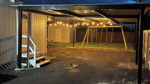 Ett takförsett utomhusområde med en gunga, ett picknickbord och ljusslingor.