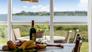 A table with a bottle of wine, fruit, and bread, overlooking a lake with a grassy landscape. - "Jurien" - 50m to the fjord by Interhome (Snedsted)