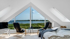A bedroom with a large window overlooking a lake, a bed, two chairs, a small table, and a TV. - "Jurien" - 50m to the fjord by Interhome (Snedsted)