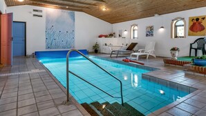 En inomhuspool med ett träbeklätt tak, en blå väggmålning och ett spaområde med ett badkar och stolar.