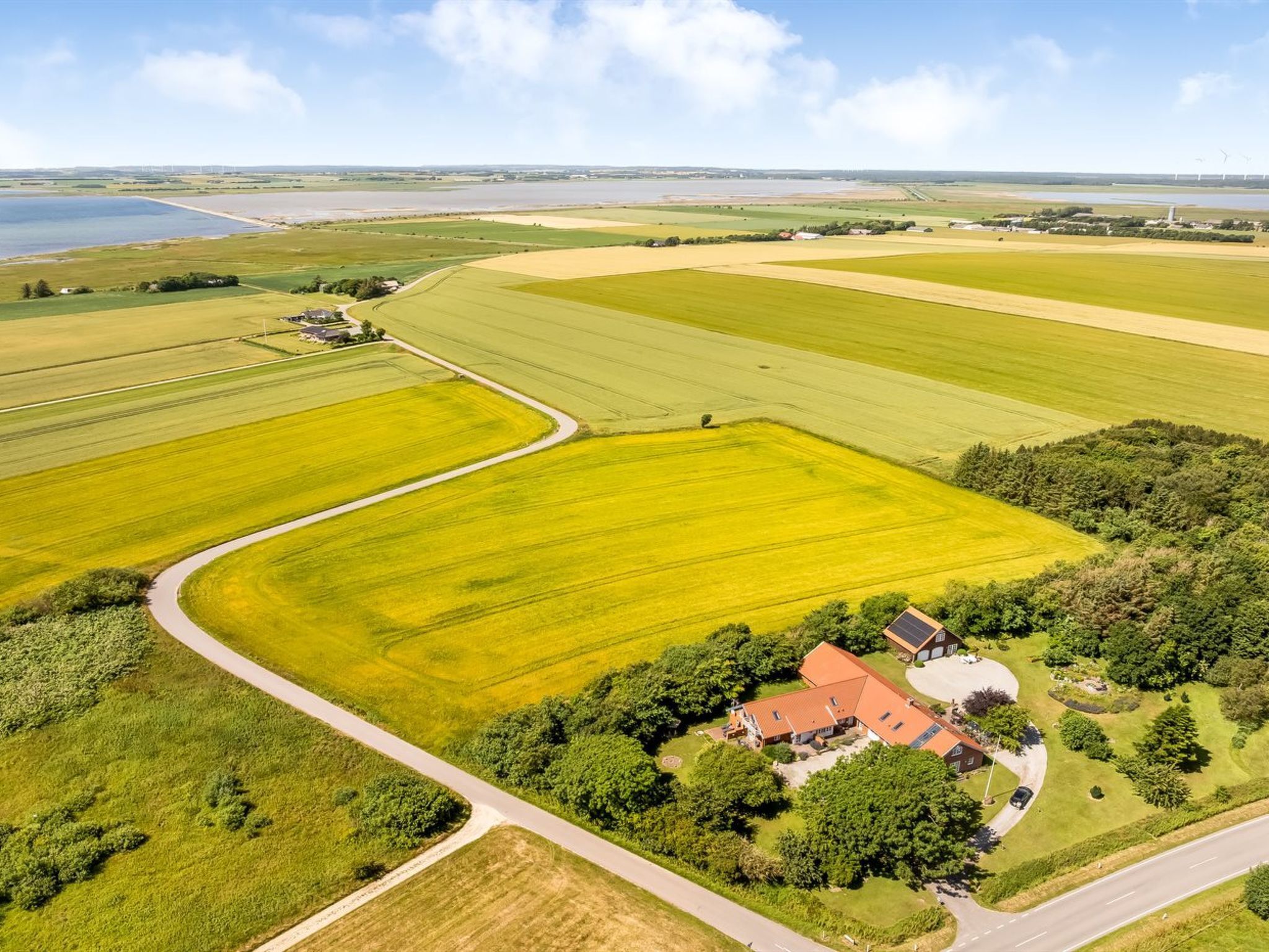 An aerial view of a rural landscape with fields, a winding road, and a house with solar panels.