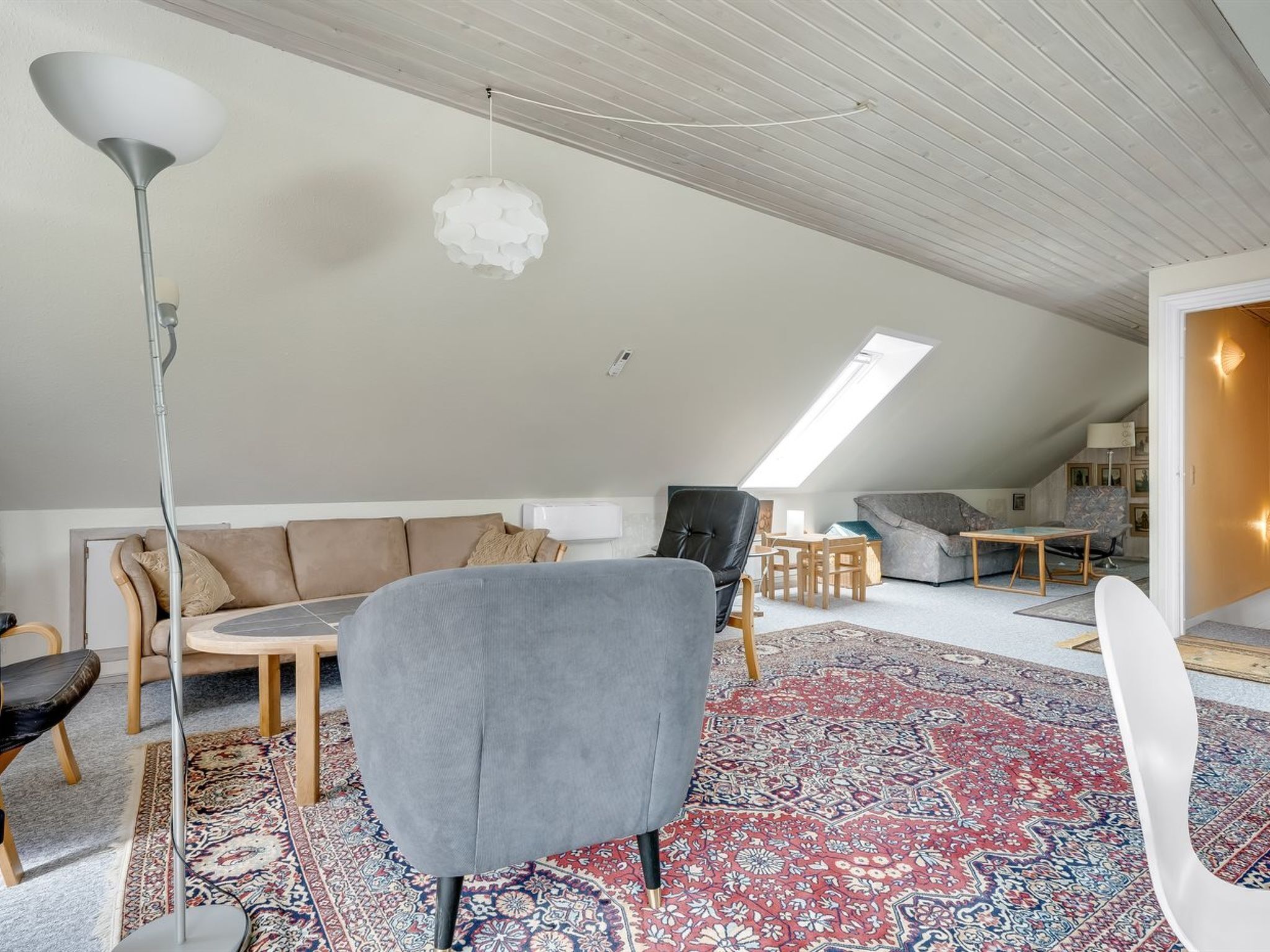 Une chambre moderne de style loft, dotée d’un plafond haut, d’un plafond en pente avec un puits de lumière, d’un canapé gris, d’une chaise noire, d’une table à manger en bois et d’un tapis à motifs.